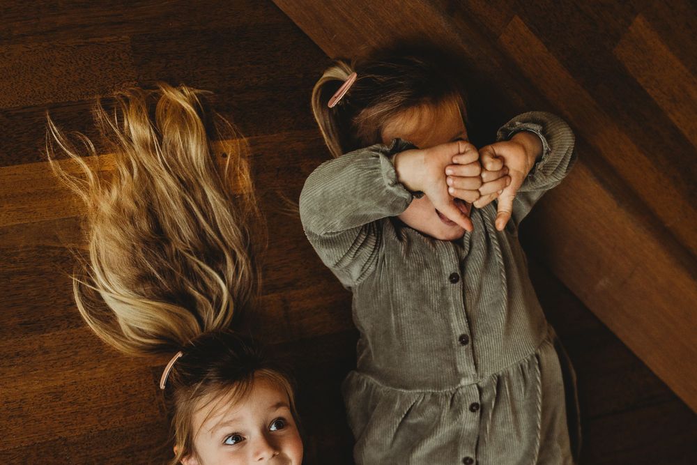 Two people lying on wooden floor playfully covering their faces with hands and hair spread out.