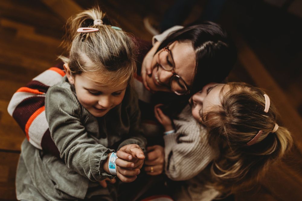 Candid moment of family members laughing and hugging on wooden floor.