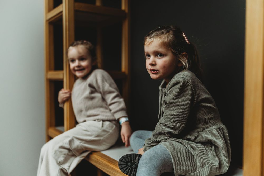 Two children in casual outfits sitting on wooden shelving unit.