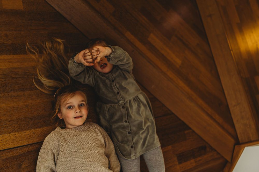 Two children laying on hardwood floor in casual attire with long hair spread out.