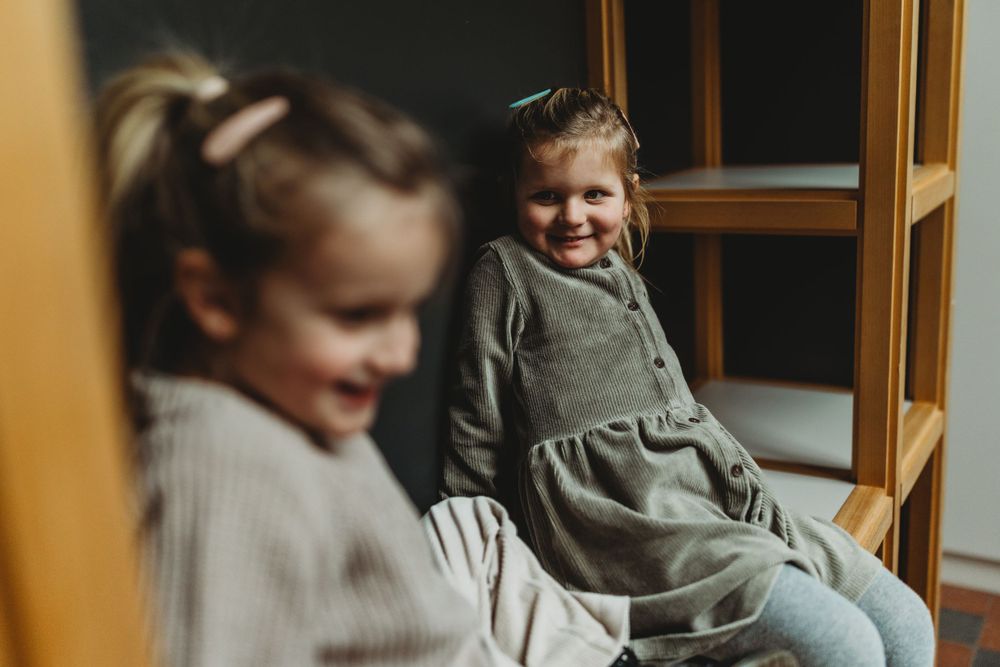 Two children sit together by a window, dressed in casual winter clothing.