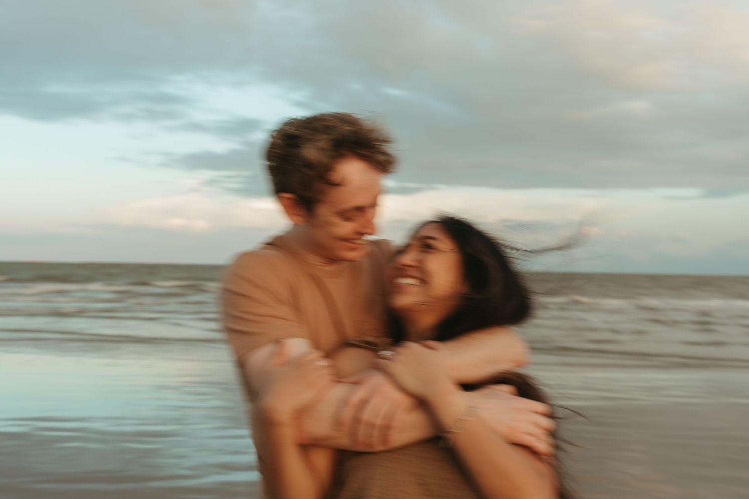 A candid moment of joy captured between a couple on a beach at dusk.