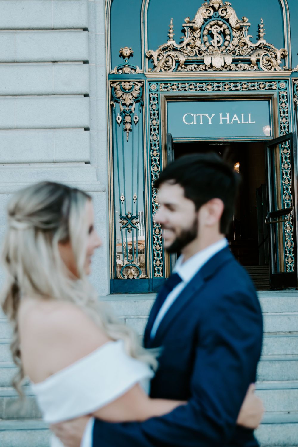 A couple stands in front of an ornate City Hall entrance with turquoise architectural details.