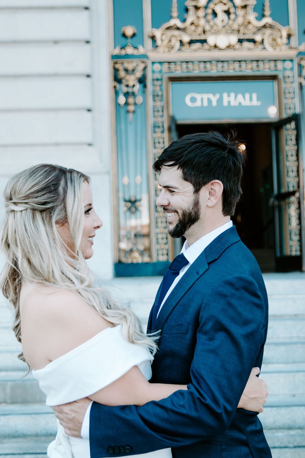 A wedding couple sharing a romantic moment outside San Francisco City Hall's ornate entrance.