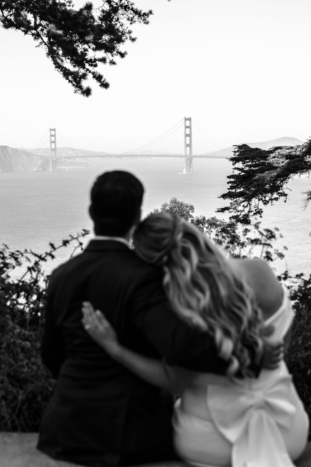 A couple admiring the Golden Gate Bridge while sitting together on a scenic overlook in San Francisco.
