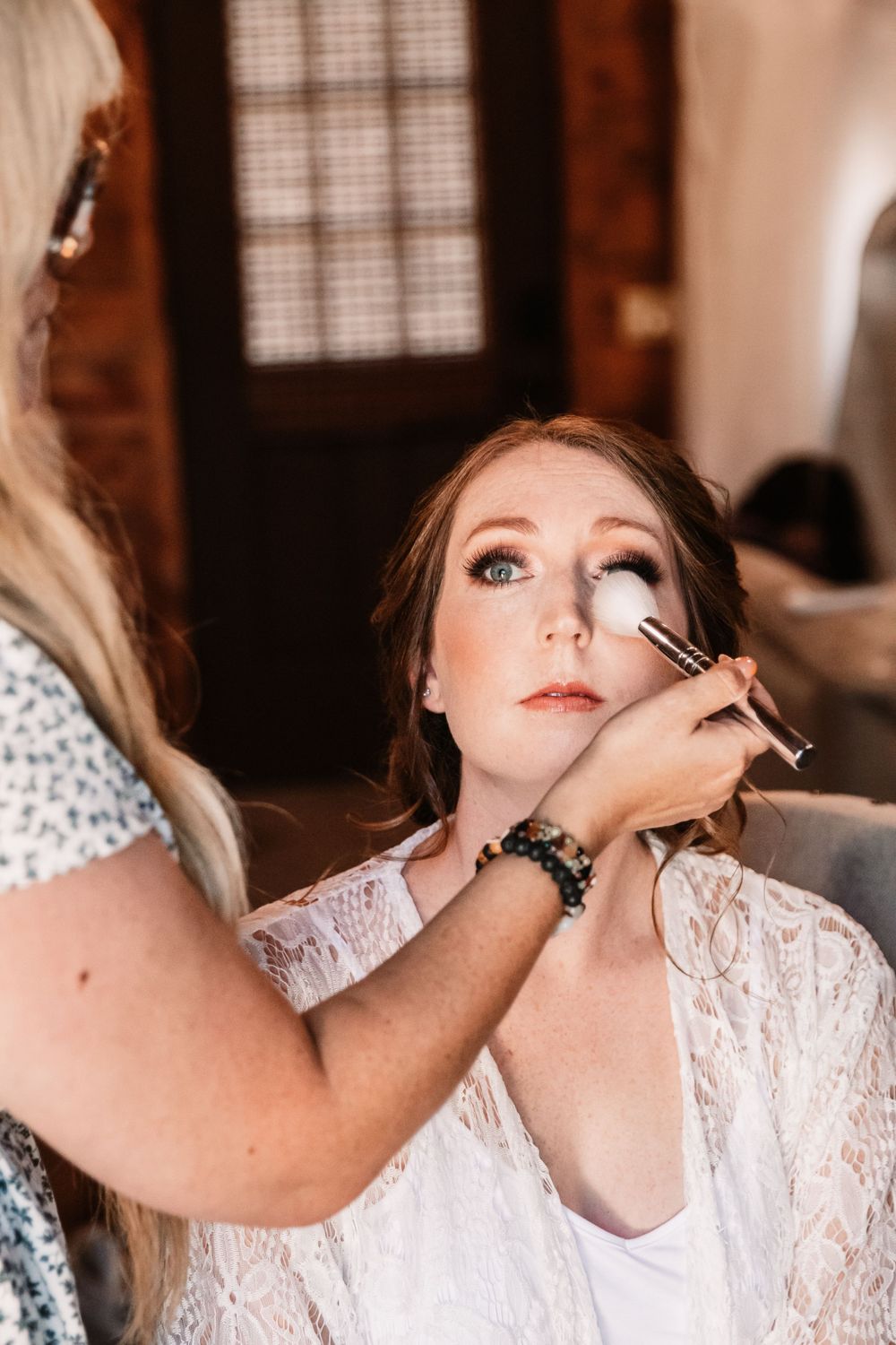Close-up shot of bridal makeup application with professional brush in soft lighting.