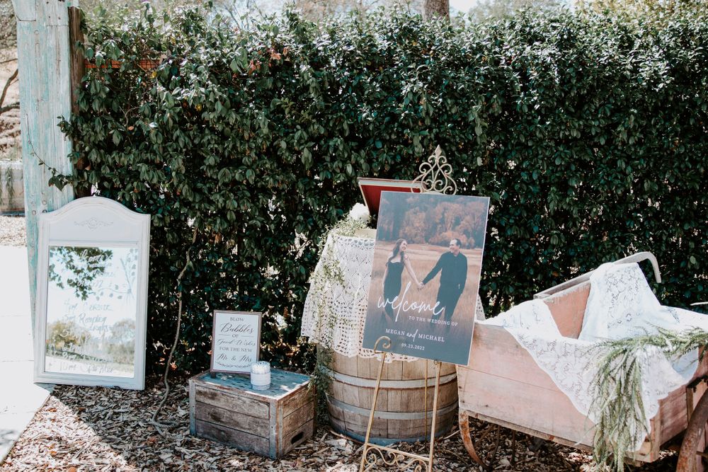 Rustic wedding decor display featuring vintage barrels and greenery against a hedge wall.