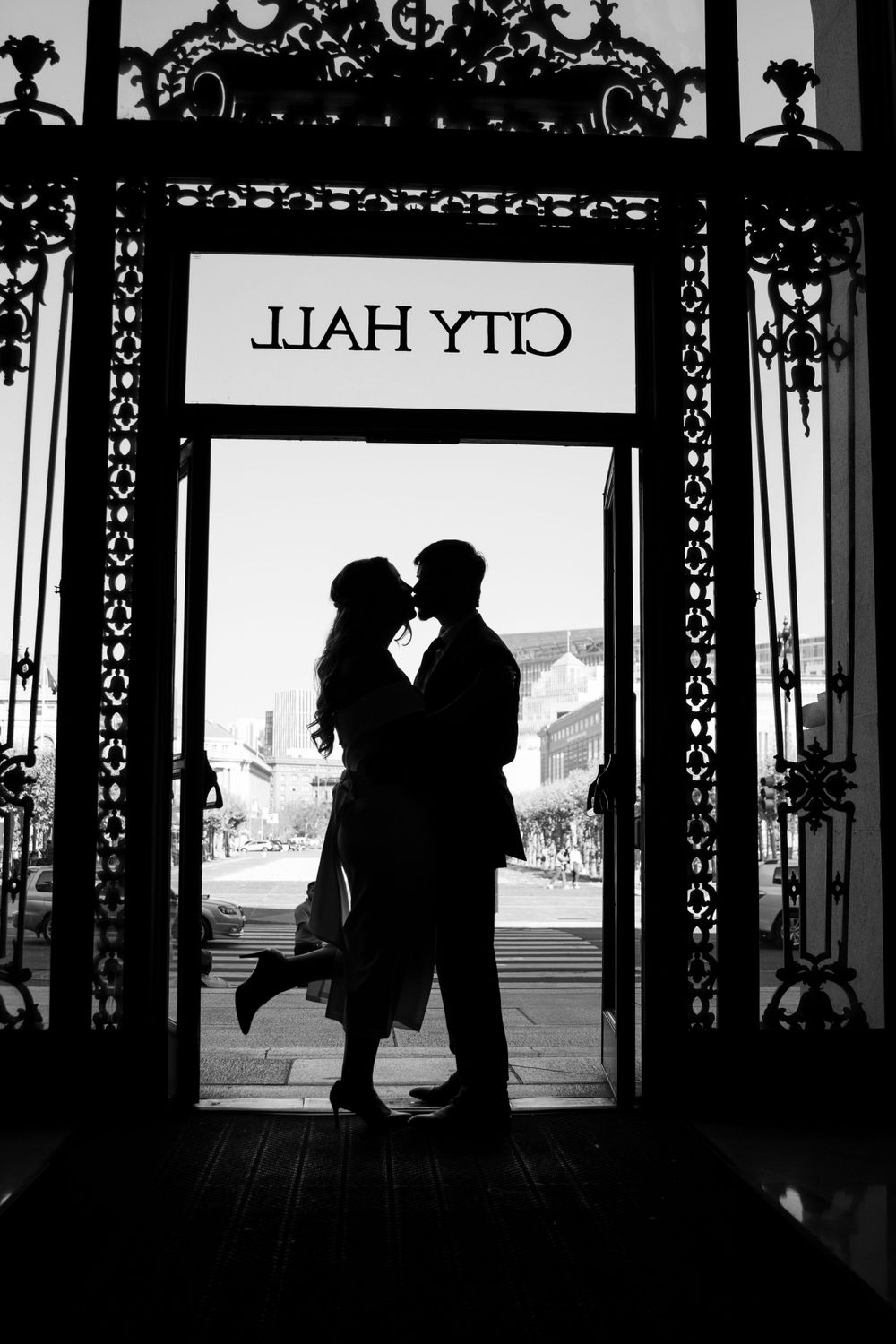 A romantic silhouette of a couple kissing under the City Hall entrance sign.