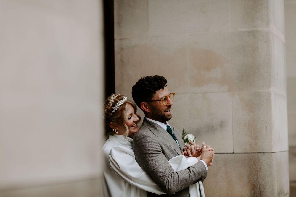A romantic moment between newlyweds against a light stone wall.