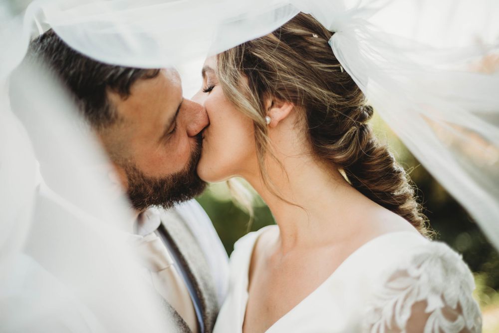"Bride and groom sharing a romantic kiss under brides veil."