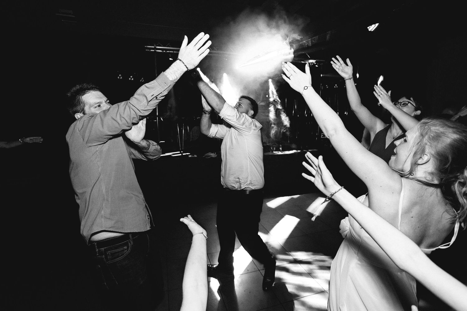 A black and white photo of people raising their hands during a wedding celebration.