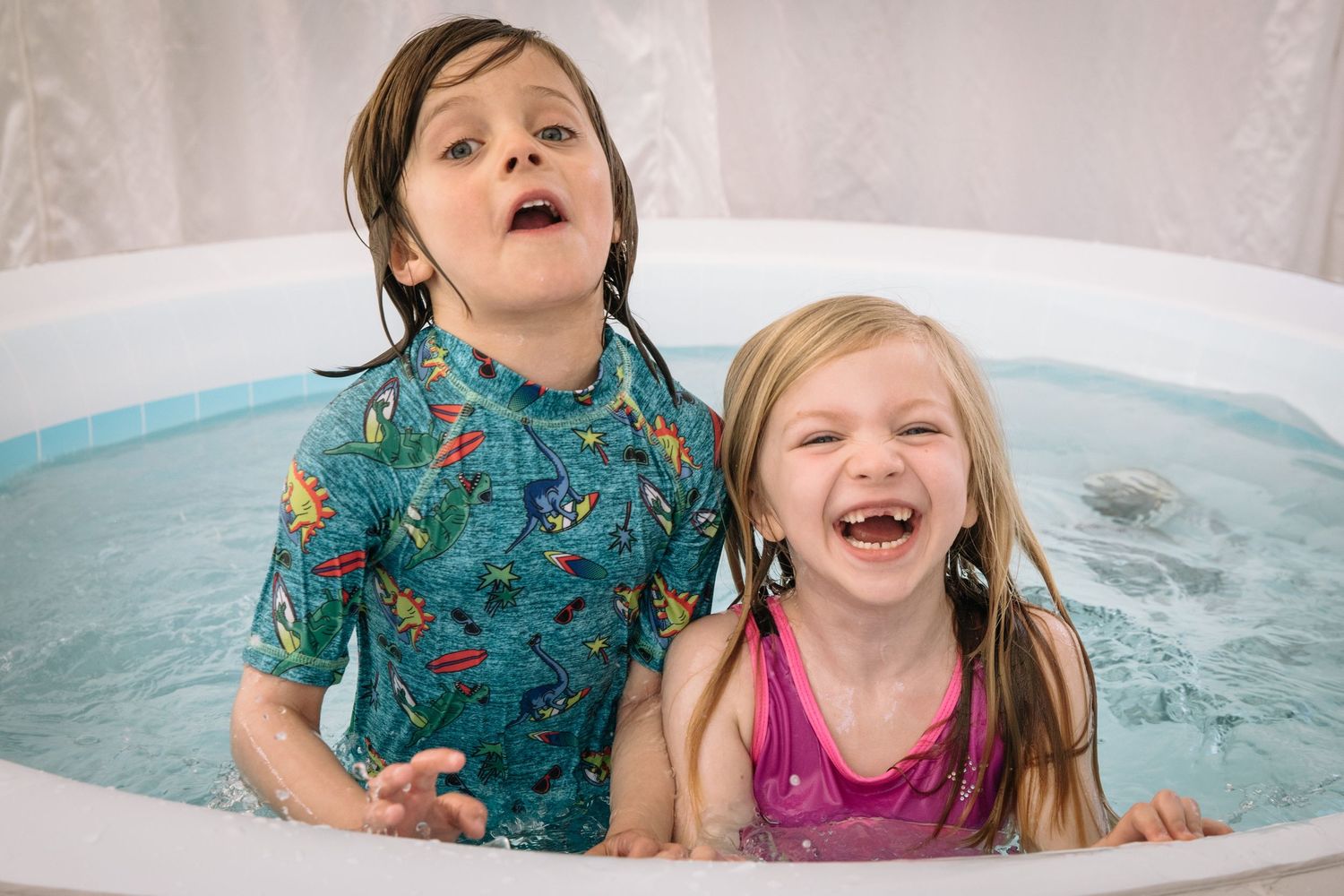 Two children laugh with joy while playing in a hot tub or inflatable pool.