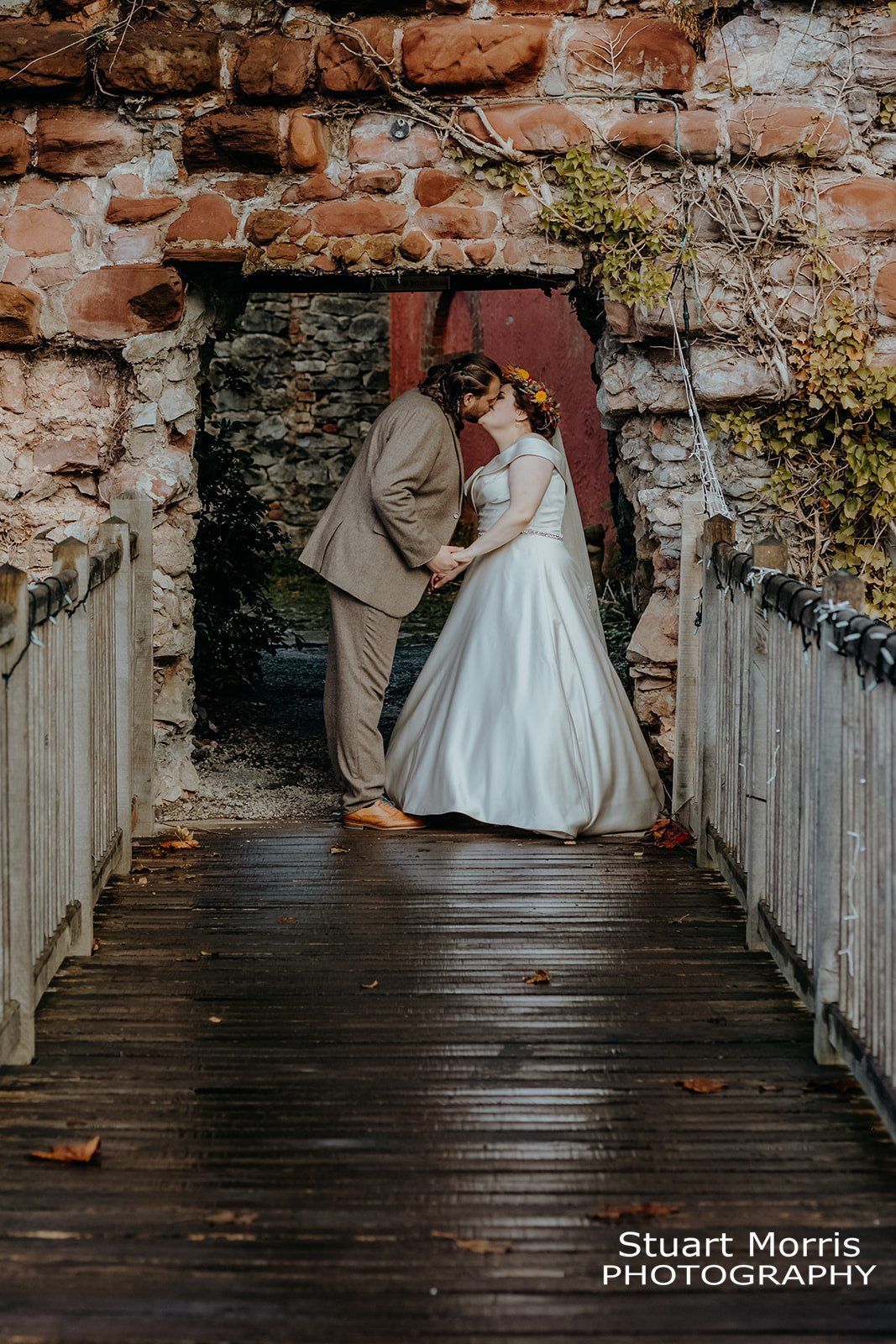 bride and groom kiss under the archway in an old stone wall in the gardens at Ruthin castle. Stuart Morris Photography