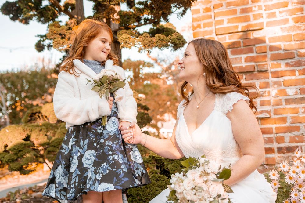 Sweet moment between bride and young girl with bouquet in autumn setting.