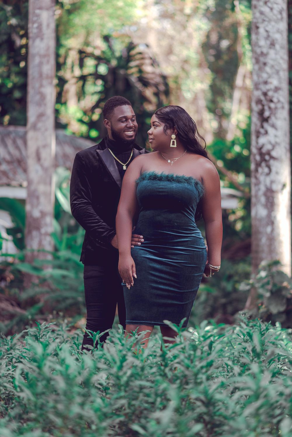 Romantic couple poses in a lush garden setting with the woman wearing an elegant teal velvet dress.