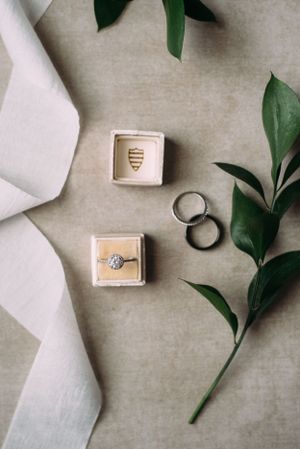 Wedding rings and jewelry boxes styled with green leaves on beige fabric.