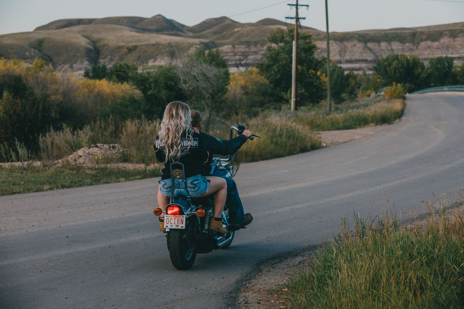 Motorcycle rider cruising on a winding rural road with hills in the background.