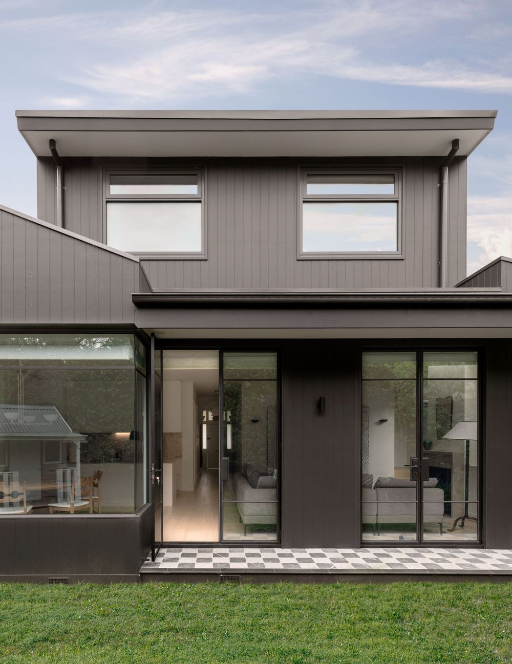 Contemporary grey house exterior with large windows and glass sliding doors opening to a grassy yard.