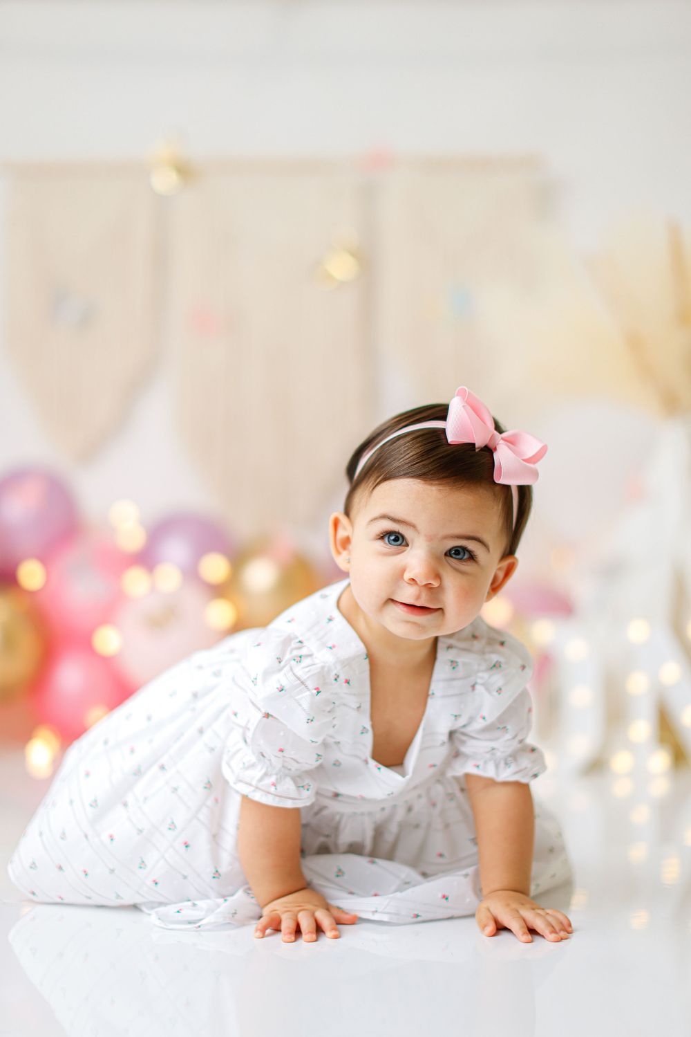 Birthday portrait with festive balloon decorations and soft lighting in white tones.