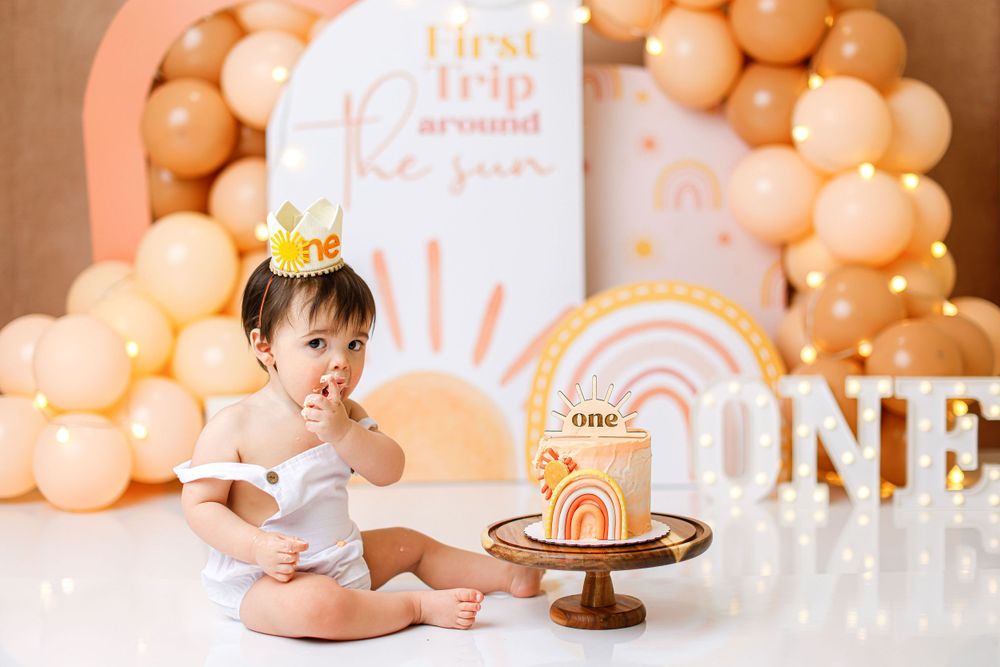 First birthday celebration setup with peach balloons and a rainbow theme cake smash scene.
