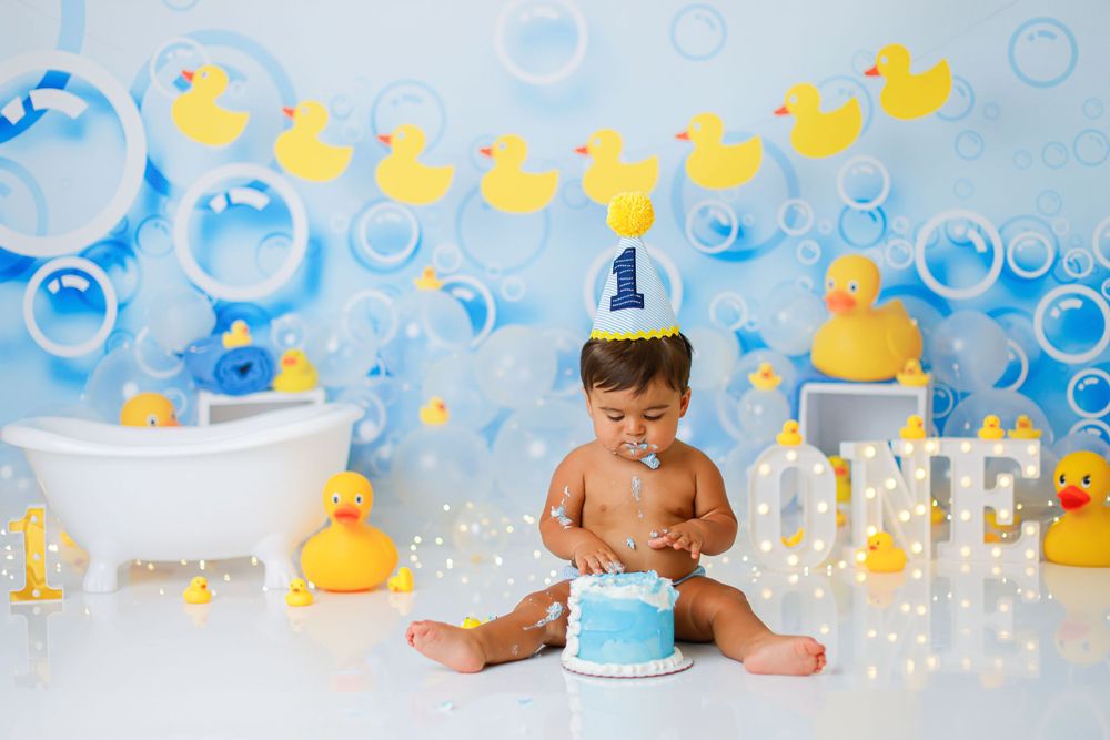 Cake smash photography setup with rubber duck theme and blue bubble decorations.