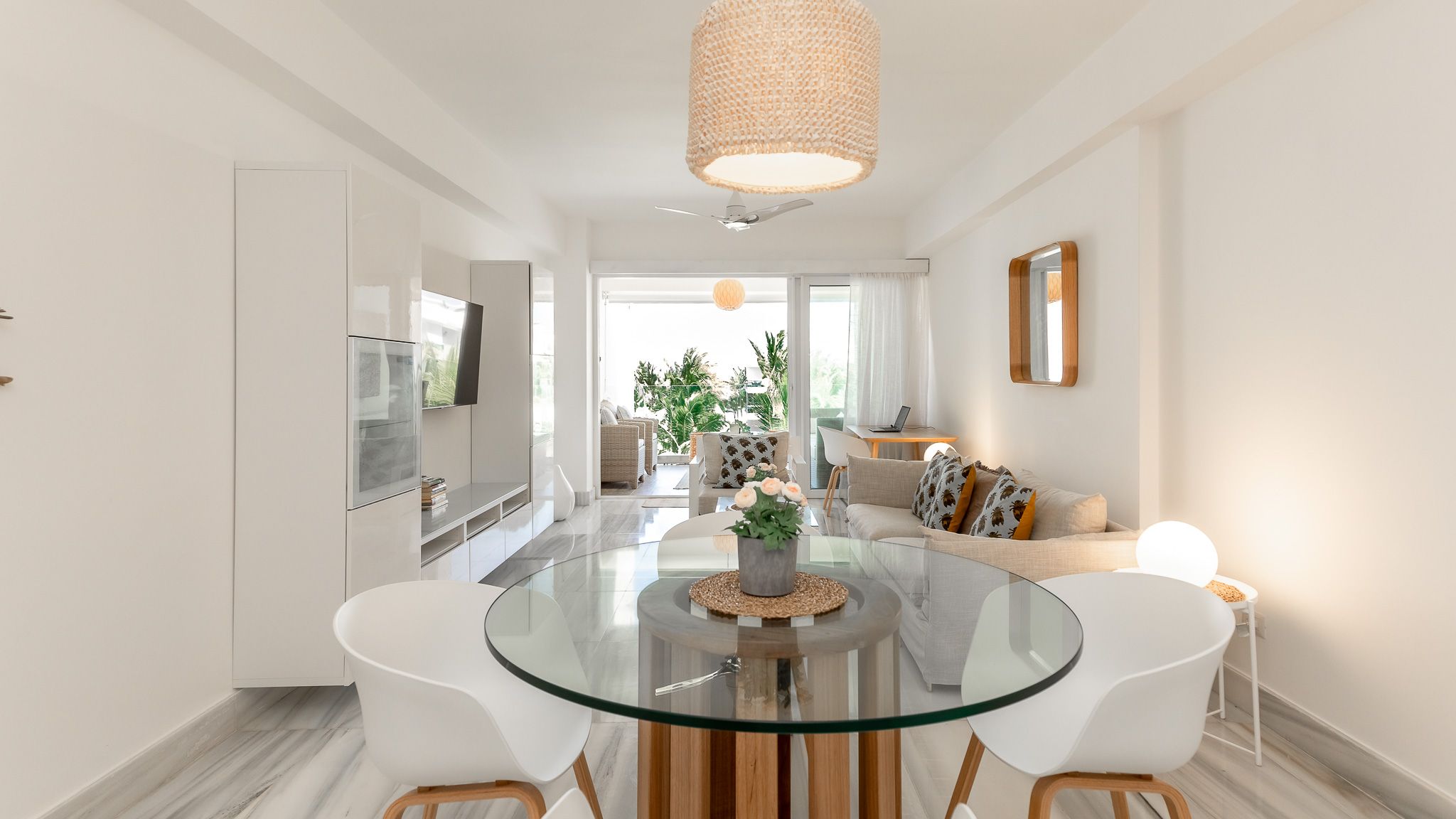 Contemporary dining space featuring glass-top table with wooden base and white chairs.