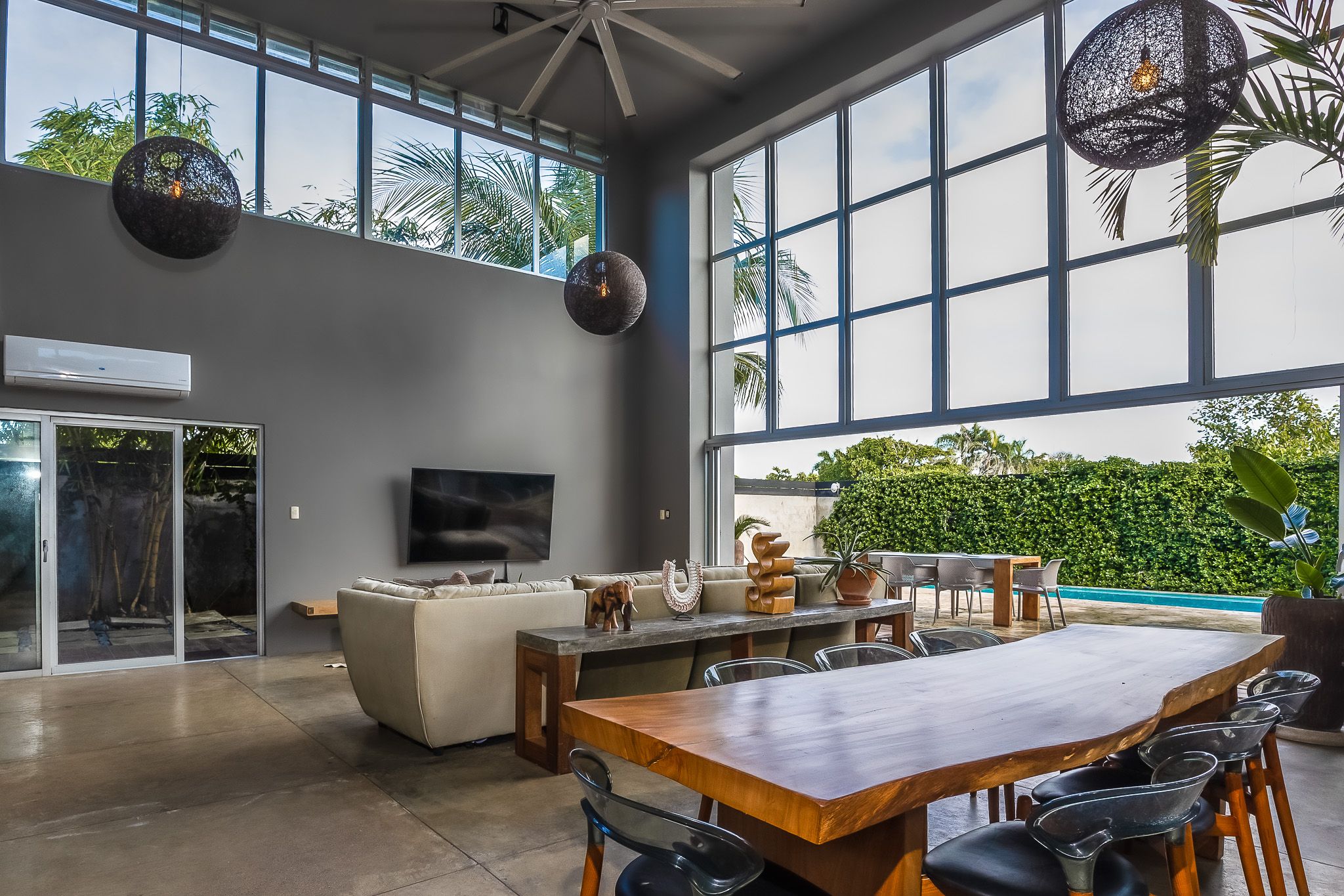 Modern living room with high ceilings, large windows, and a wooden dining table complemented by hanging globe lights.