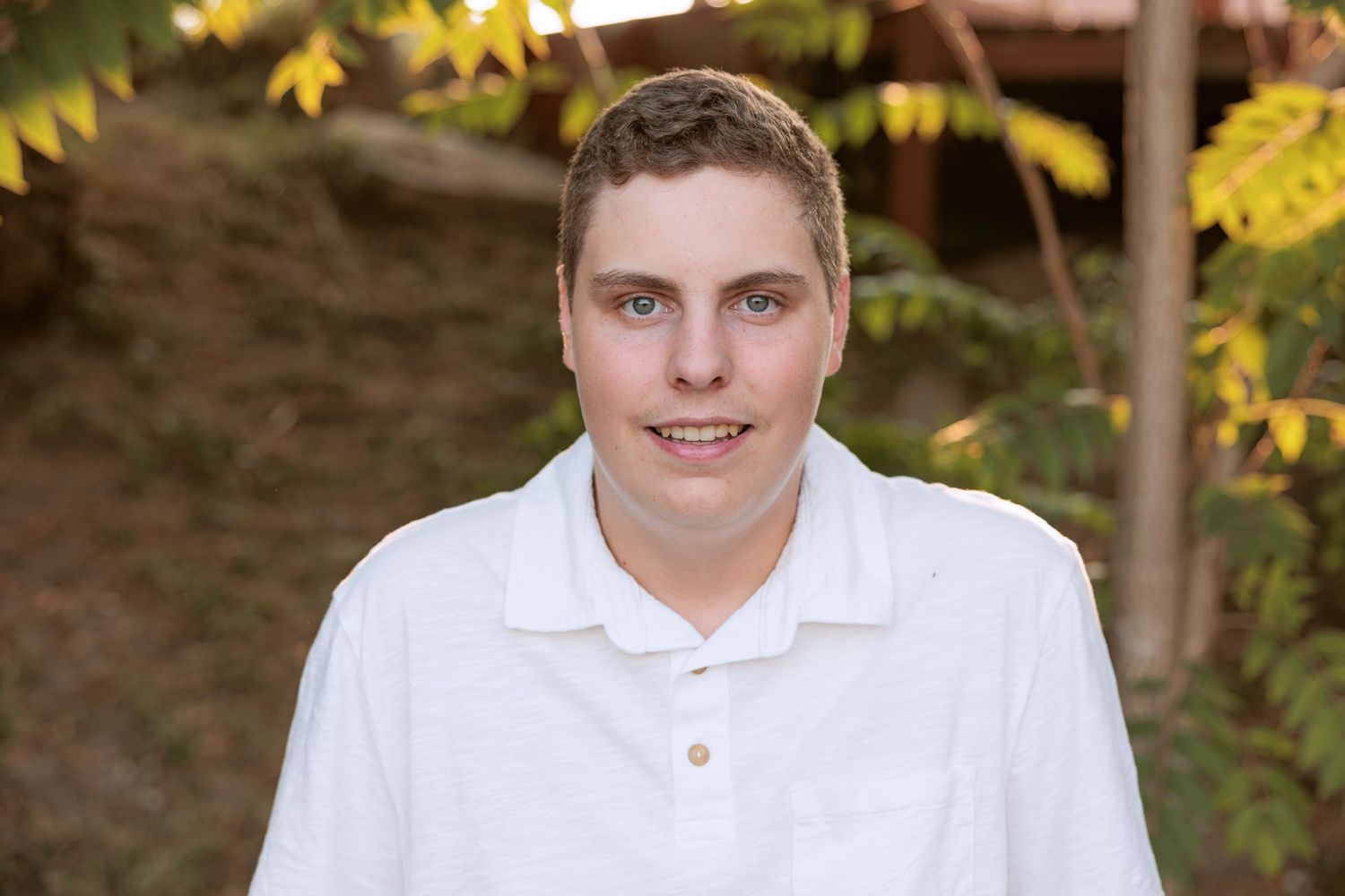 An outdoor portrait featuring someone in a white polo against an autumn background.