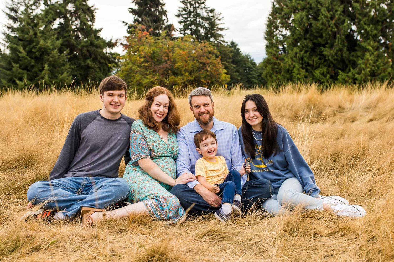 Seated portrait of a smiling family in a grassy field in Woodinville