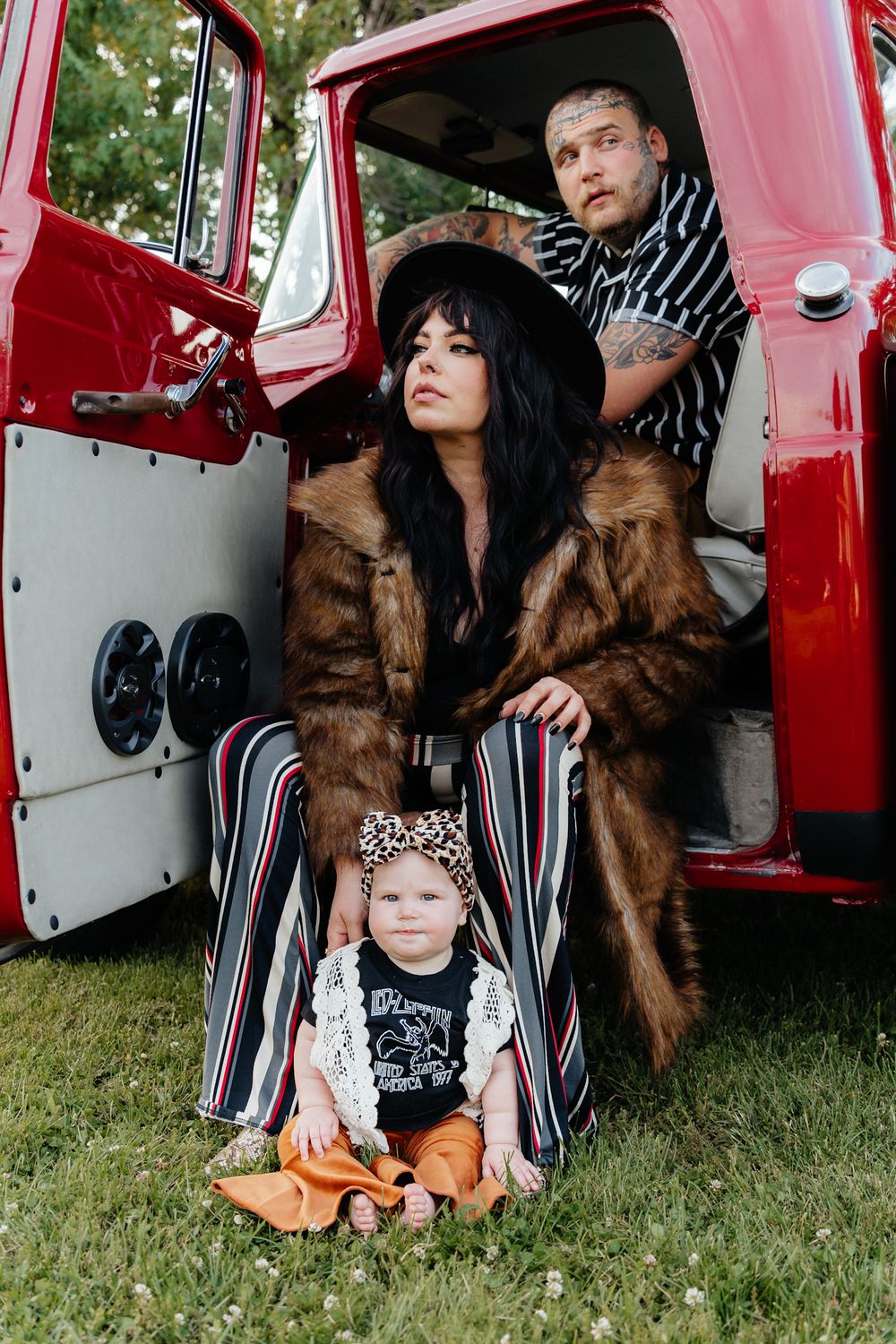 Happy couple with their baby sitting on the ground in front of a vintage red truck that belong's to their grandfather