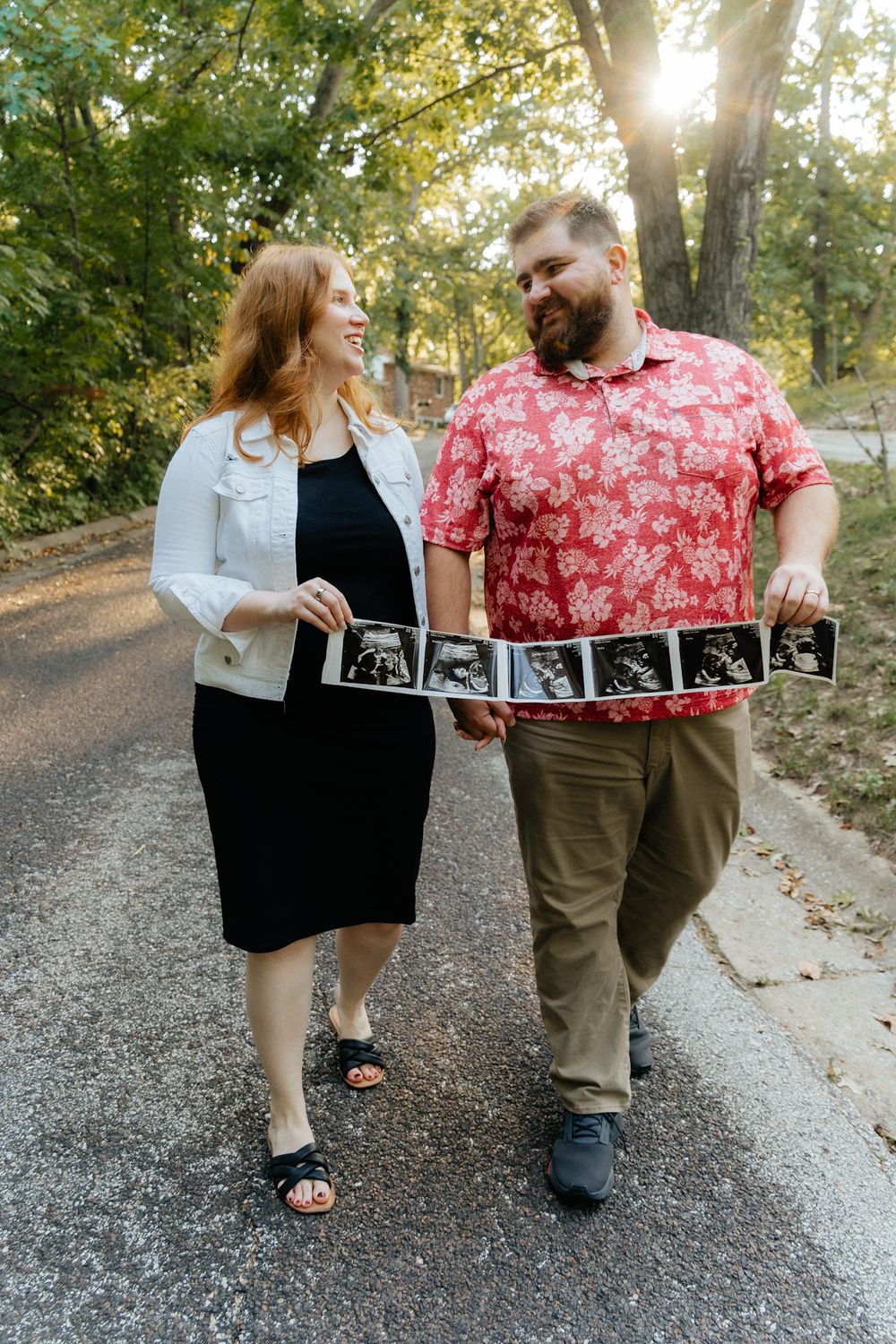 Couple walking together while holding up their ultrasound images, smiling and announcing their pregnancy with excitement