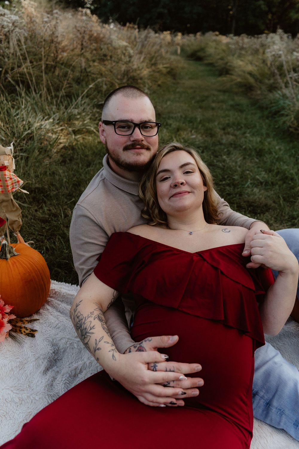 Expecting couple sitting on a blanket next to pumpkin, with the couple looking excited for their upcoming arrival
