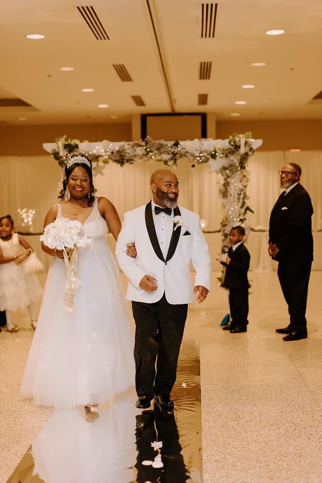 Wedding ceremony recessional in reception hall with floral arch and white decor.