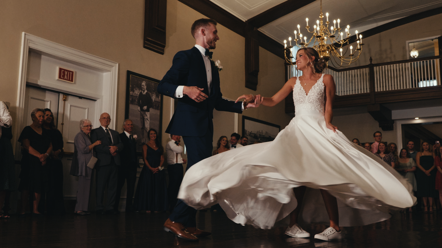 A couple performs their first dance in an elegant ballroom with chandeliers.