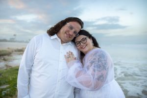 A couple embraces on a beach during sunset wearing matching white outfits.