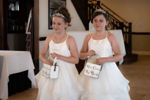 Two flower girls in white dresses carrying baskets walk together during a wedding ceremony.