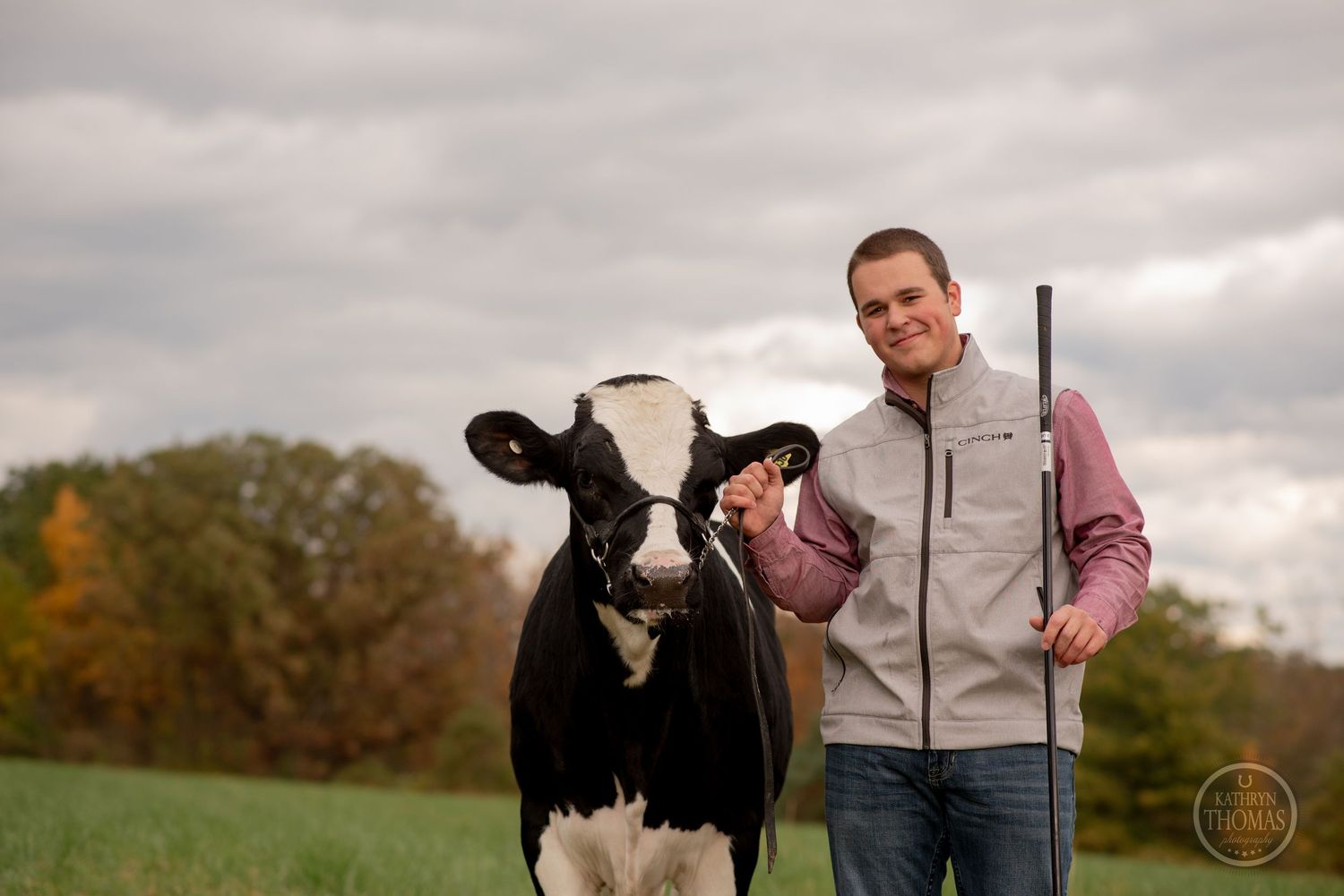 Person in casual attire stands confidently in autumn field during overcast day.