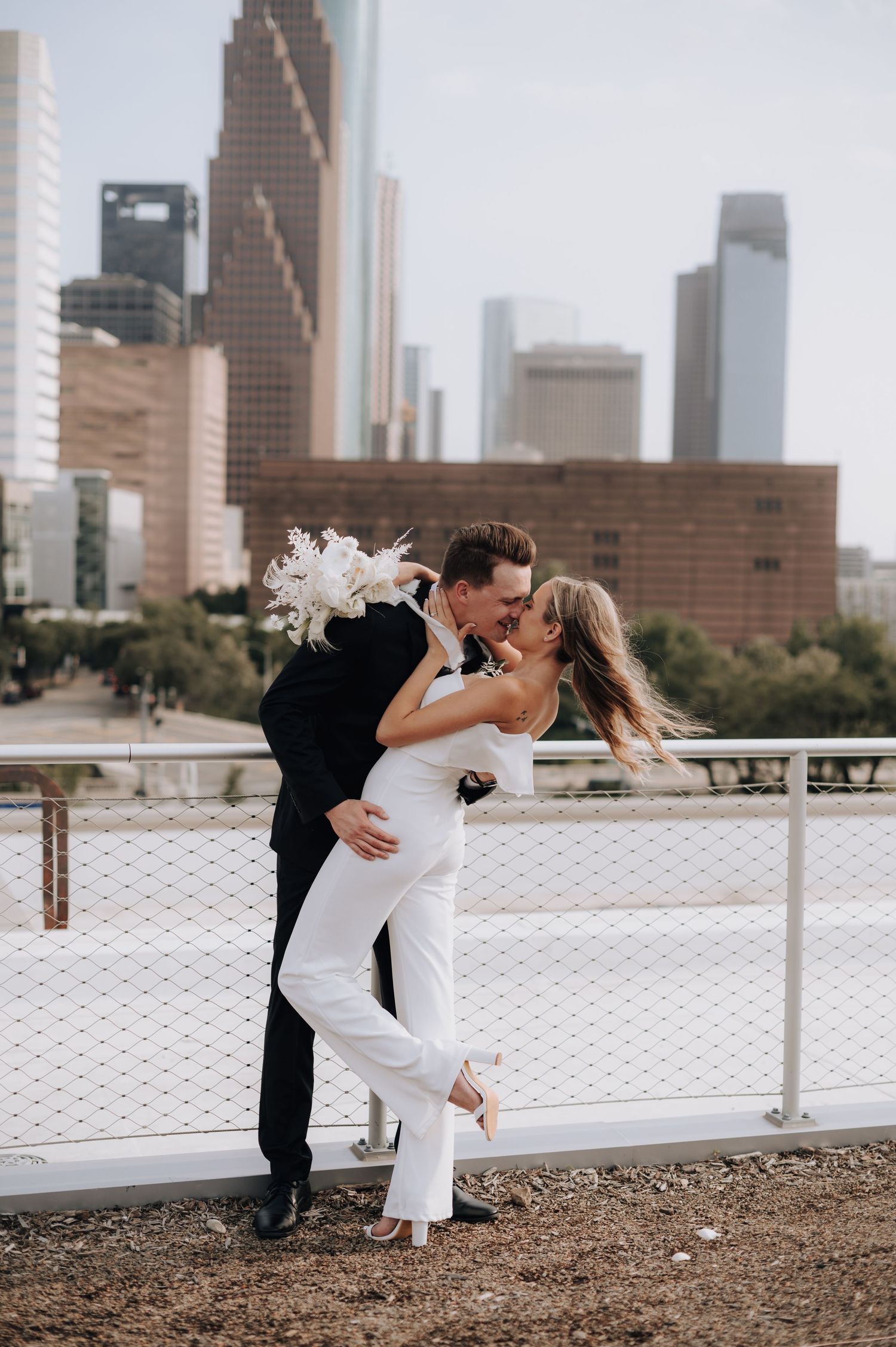 Romantic dip kiss with Houston skyline in background during wedding photoshoot.