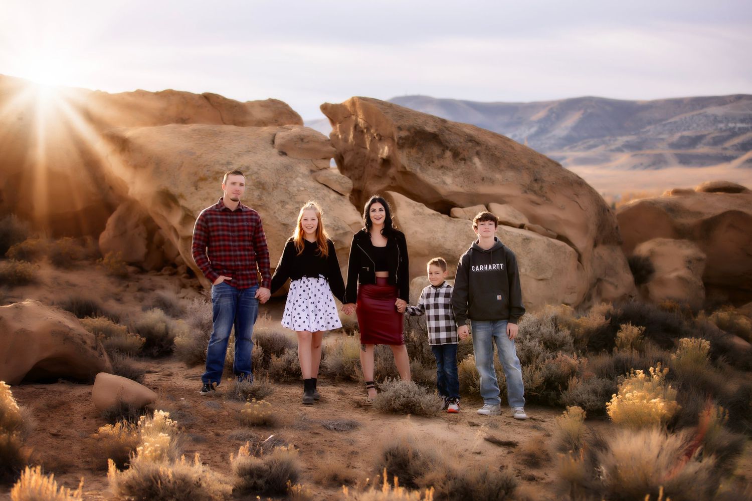 A family poses together against red rock formations at sunset in a desert landscape.