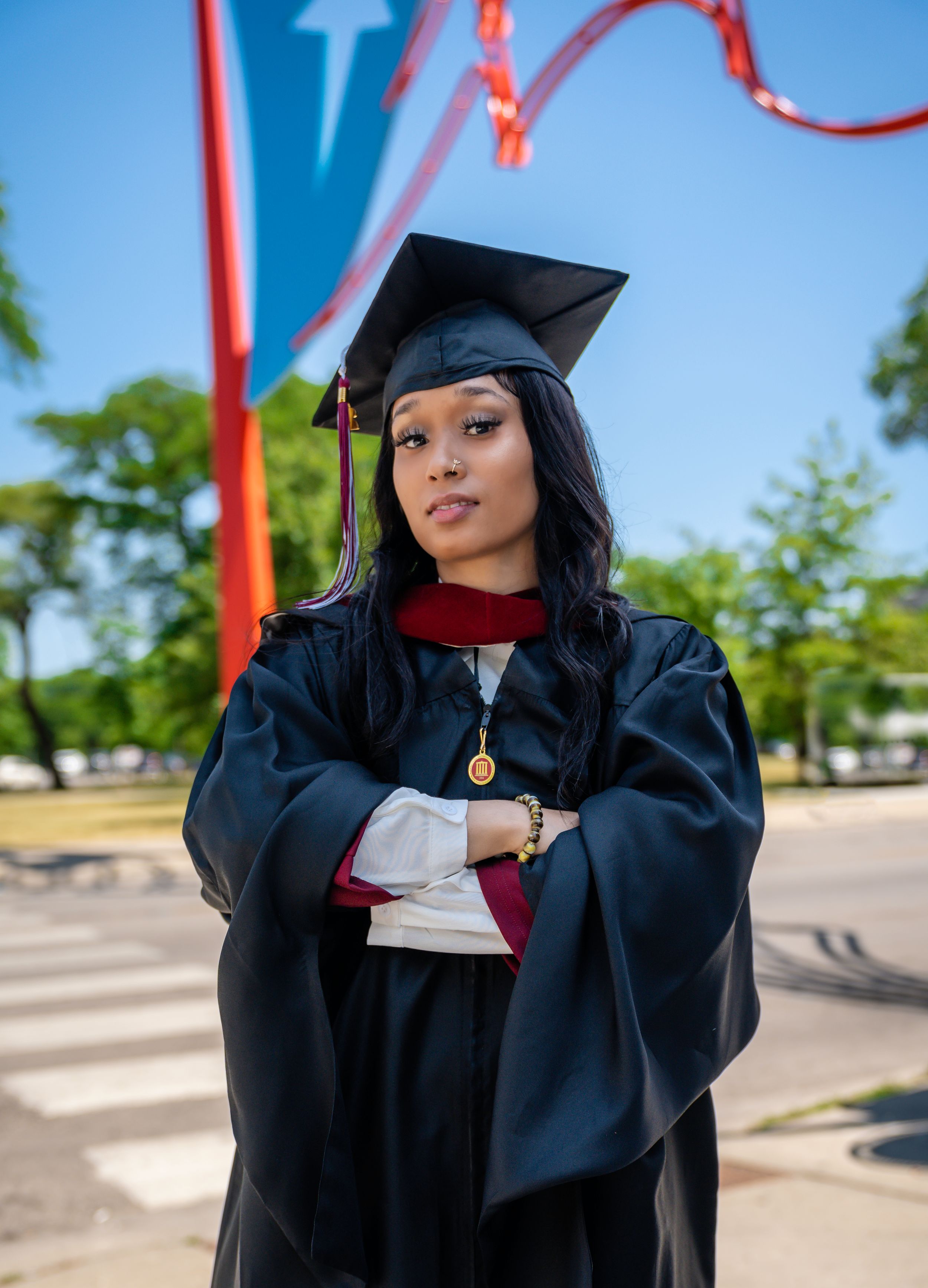 Academic graduation photoshoot outdoors featuring black cap and gown against a bright blue sky.