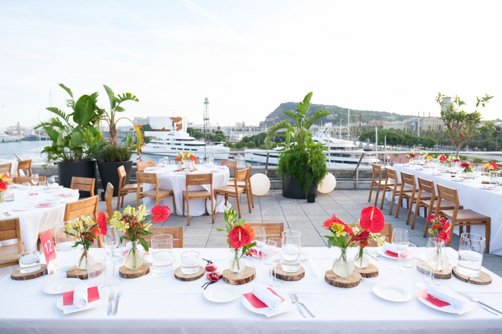 Elegant outdoor dining setup with white tablecloths and floral centerpieces at a waterfront venue.