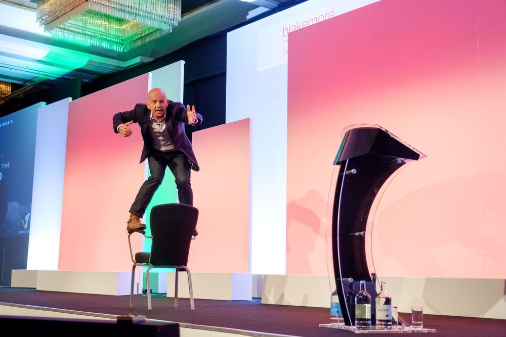 Dynamic speaker performs energetically on stage with colorful backdrop during presentation.