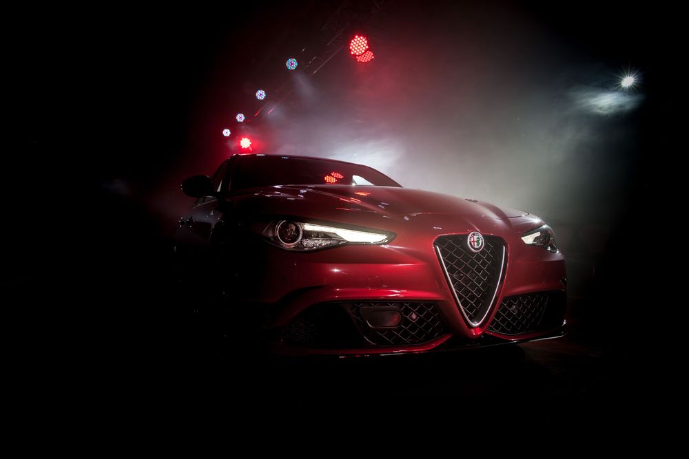 Red Alfa Romeo sports car dramatically lit in dark showroom setting.