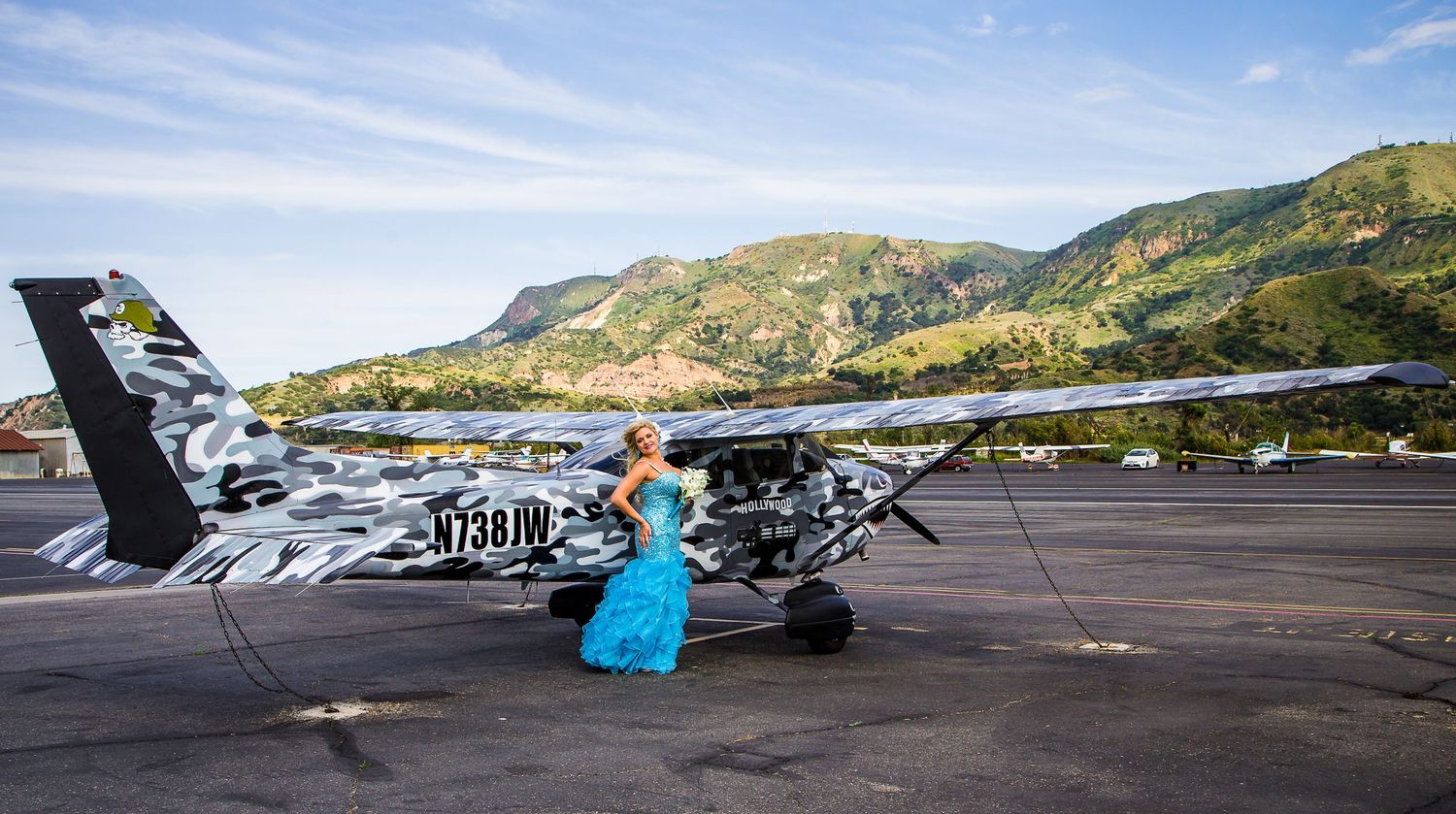 Radiant bride standing gracefully in front of a camouflaged plane, with majestic mountains providing a stunning backdrop