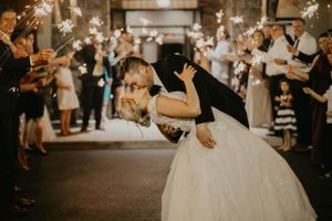 Romantic wedding sparkler exit with couple sharing dramatic dip kiss surrounded by guests.