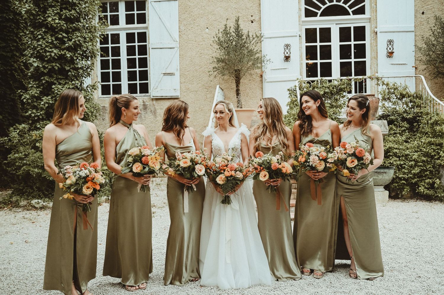 Bridesmaids in sage green dresses hold colorful bouquets while posing with bride.