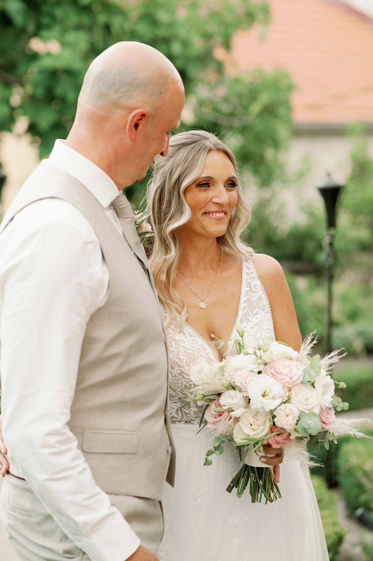 Elegant wedding couple sharing a tender moment in a garden with a white floral bouquet.