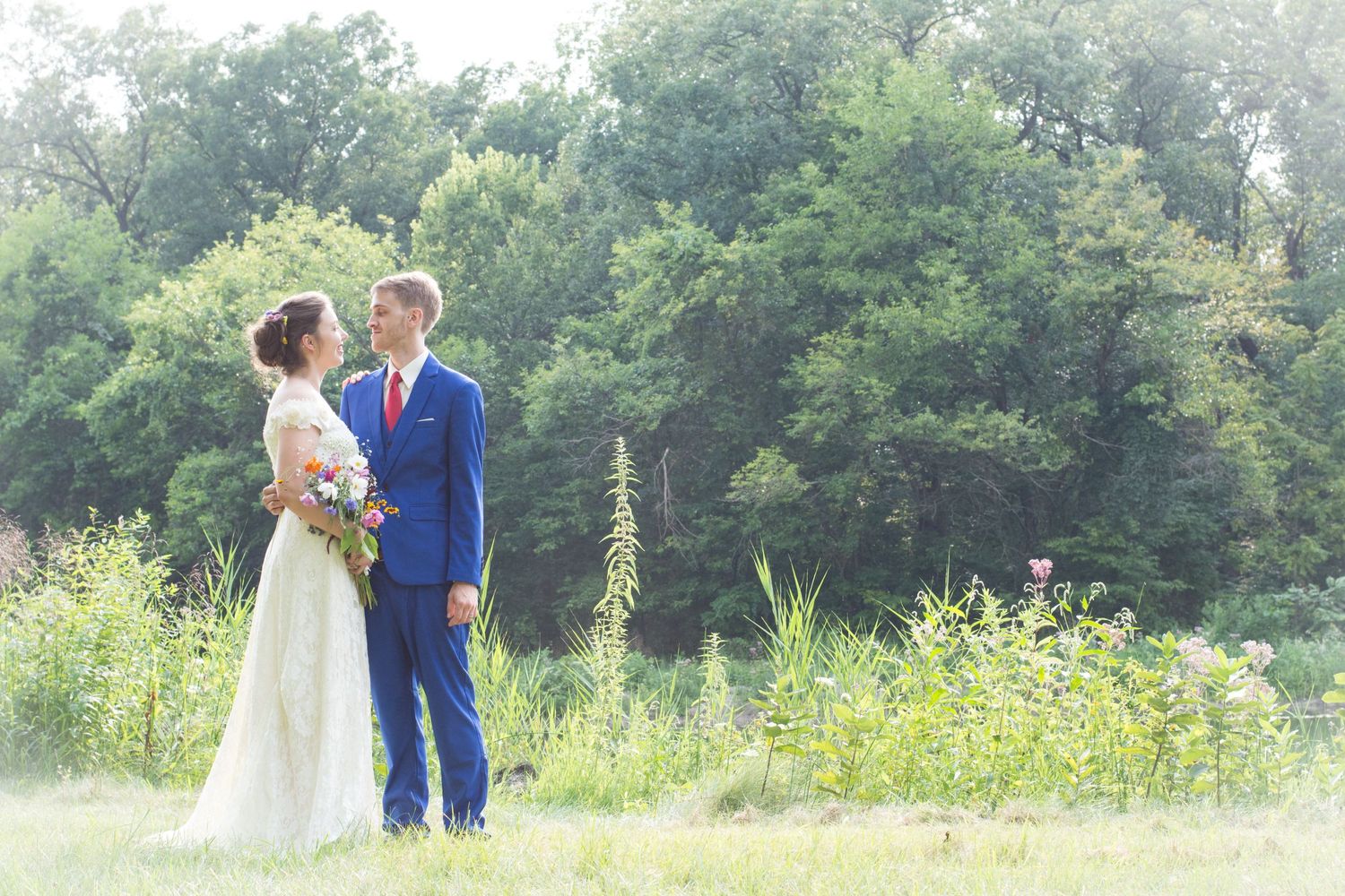 Ethereal outdoor wedding photo with couple standing in a sun-drenched meadow with wildflowers.