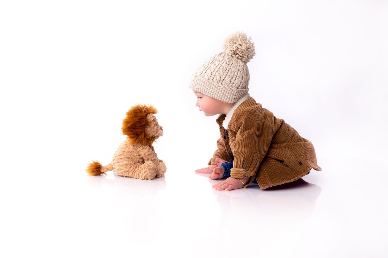Child in winter attire sitting and playing with a teddy bear on white background.