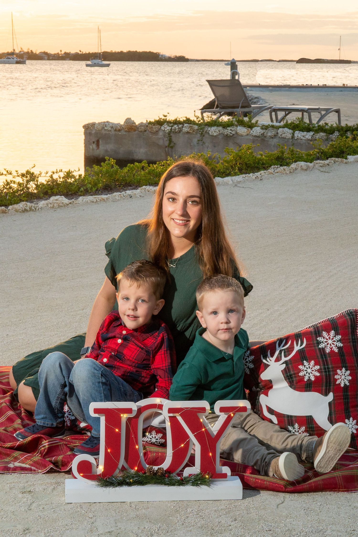 Family photo session at sunset with festive JOY letters on beach setting.
